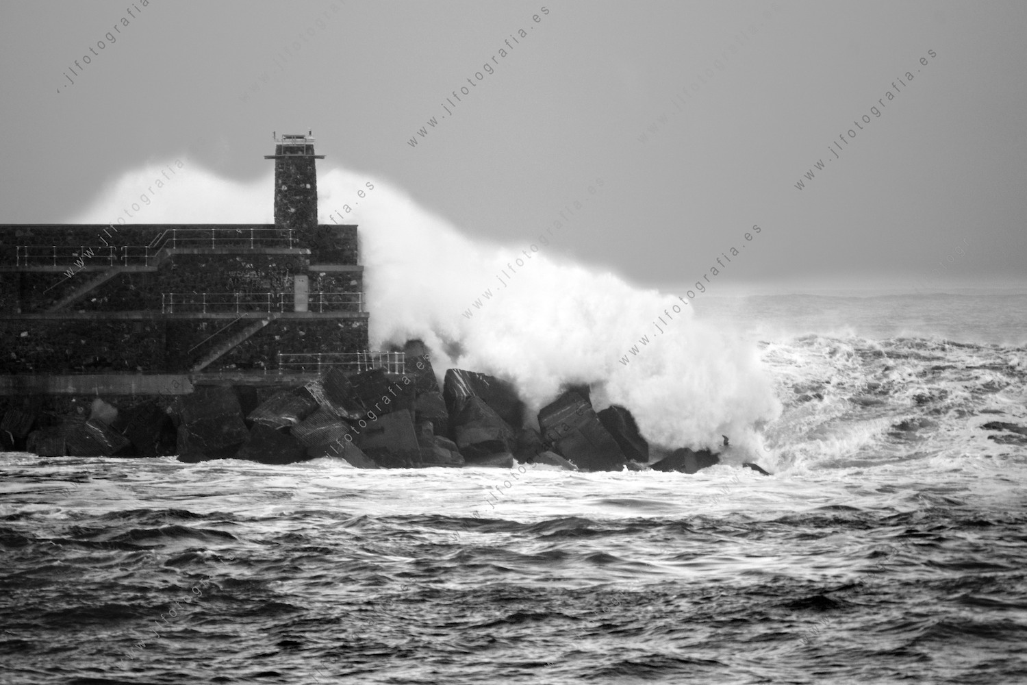 Una ola gigante, rompe y pasa por encima del dique y el faro del puerto de Bermeo