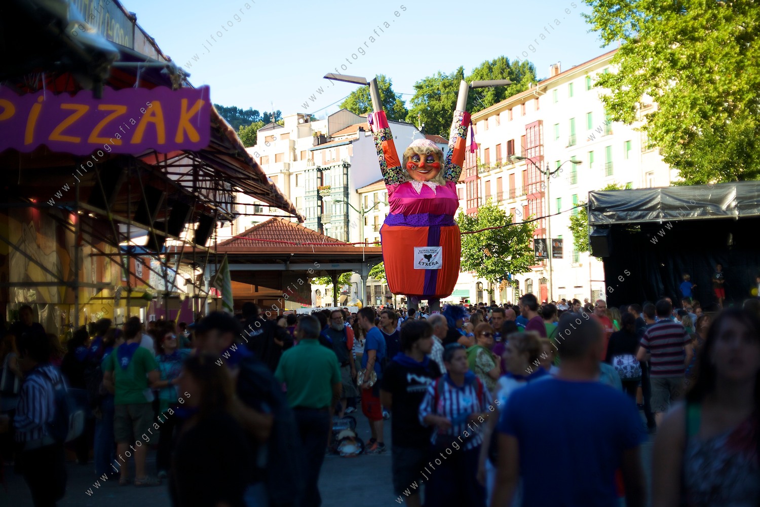 Aste Nagusia de Bilbao, en las txoznas, una gran Marijaia luce aprovechando ingeniosamente dos farolas del Arenal