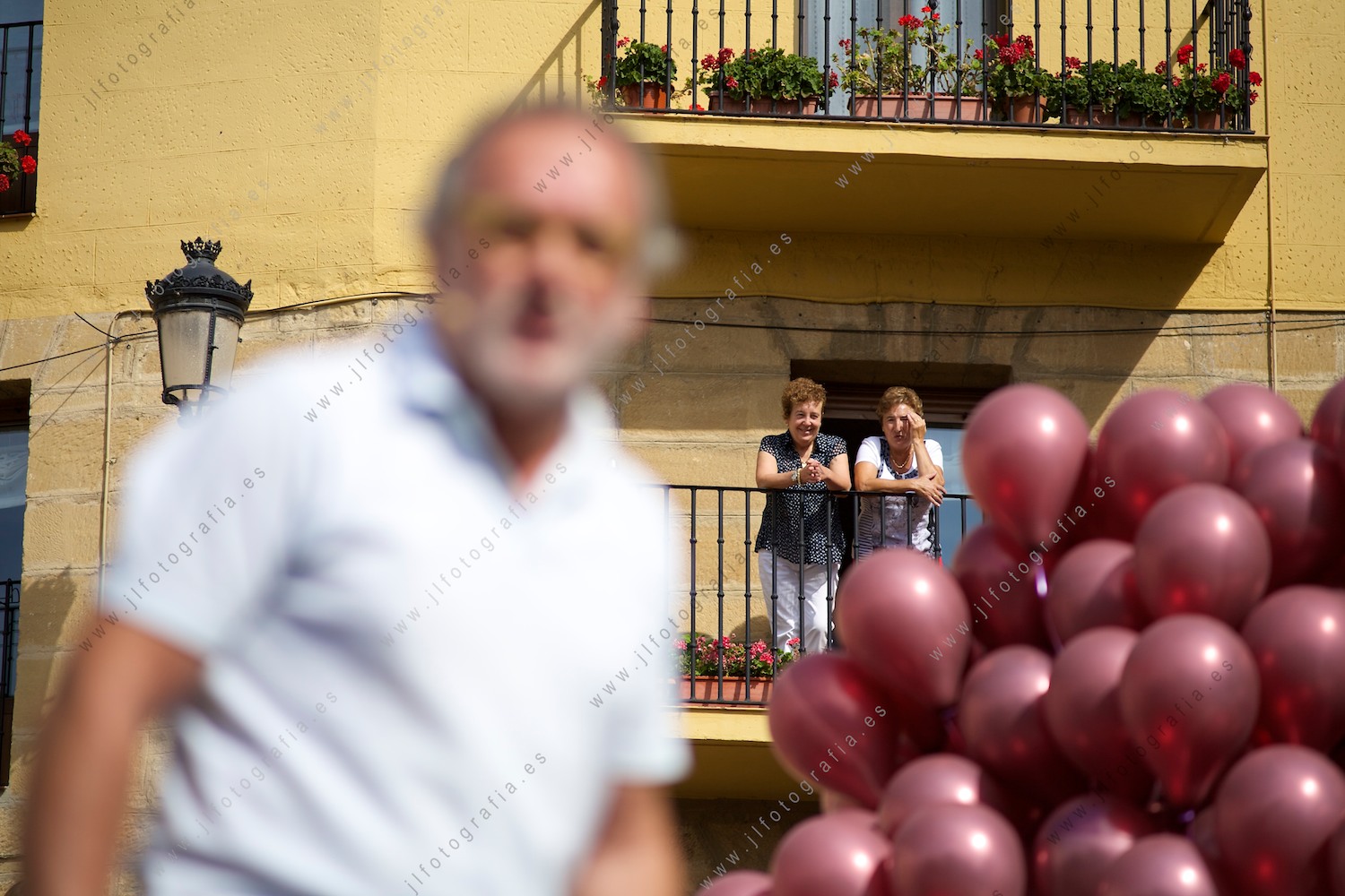 Dos señoras miran desde su balcón en Labastida al presentador de la fiesta del vino