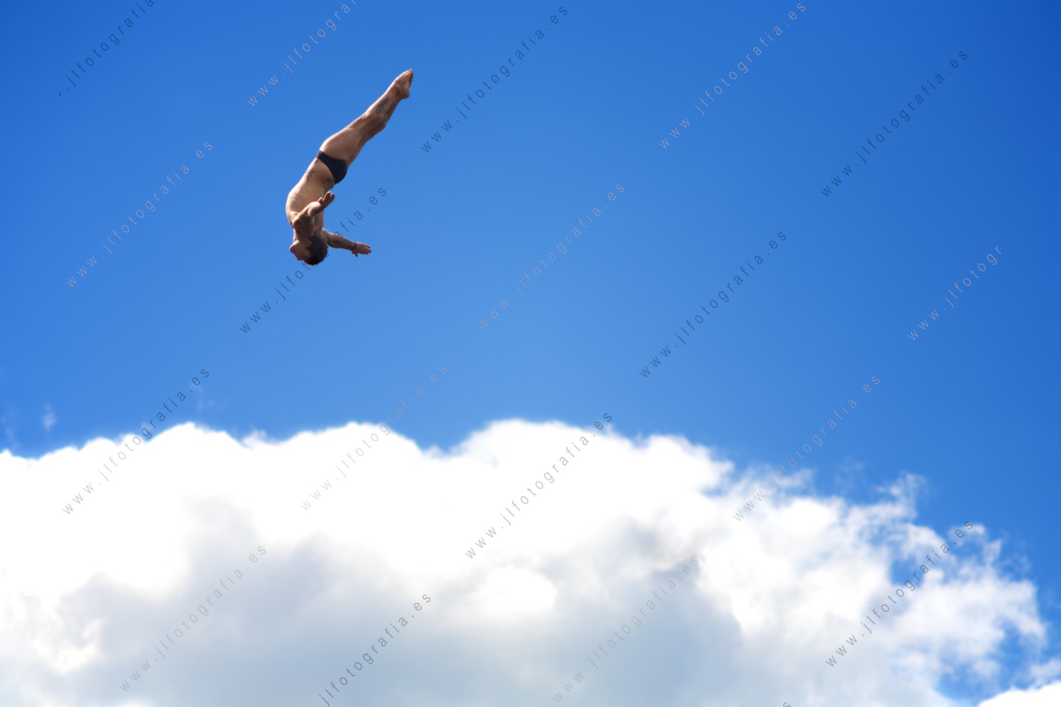 salto en posición picada de un clavadista Cliff Diving de Red Bull con las nubes de fondo