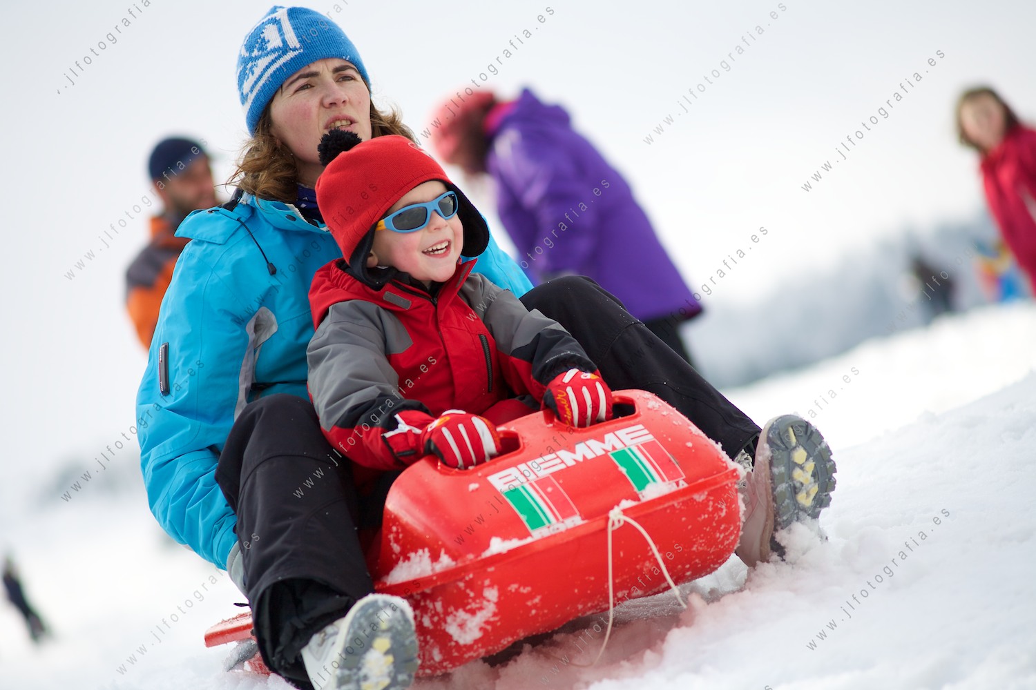Madre con su niño en un trineo de nieve a punto de descender por la ladera