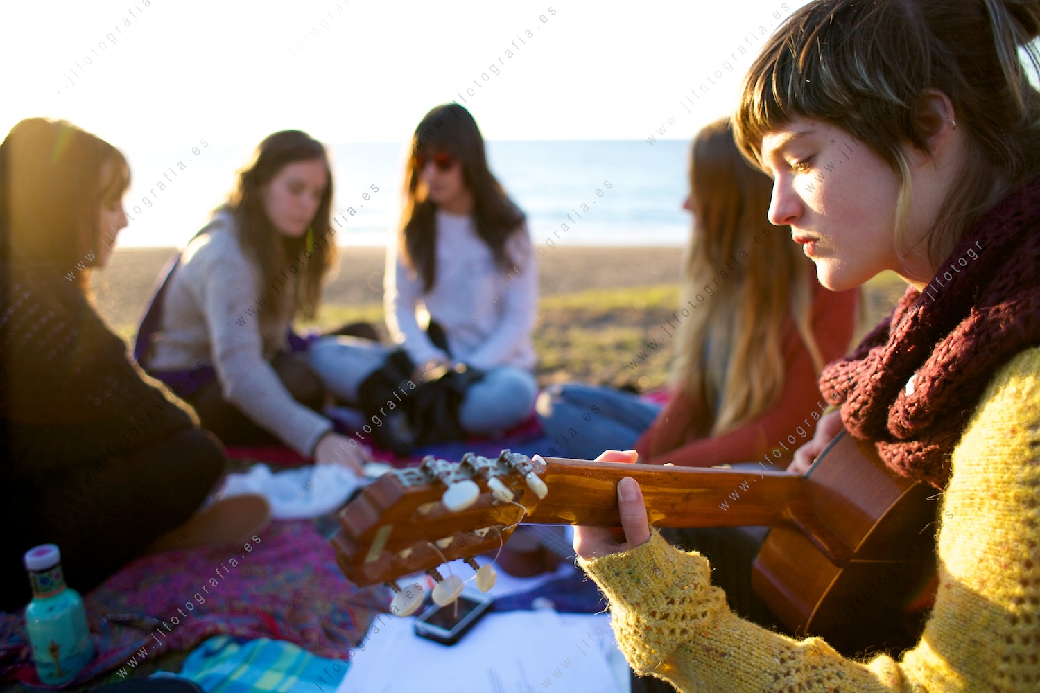 Plano de detalle de una joven tocando la guitarra junto al grupo de amigas, en la playa de Azkorri.