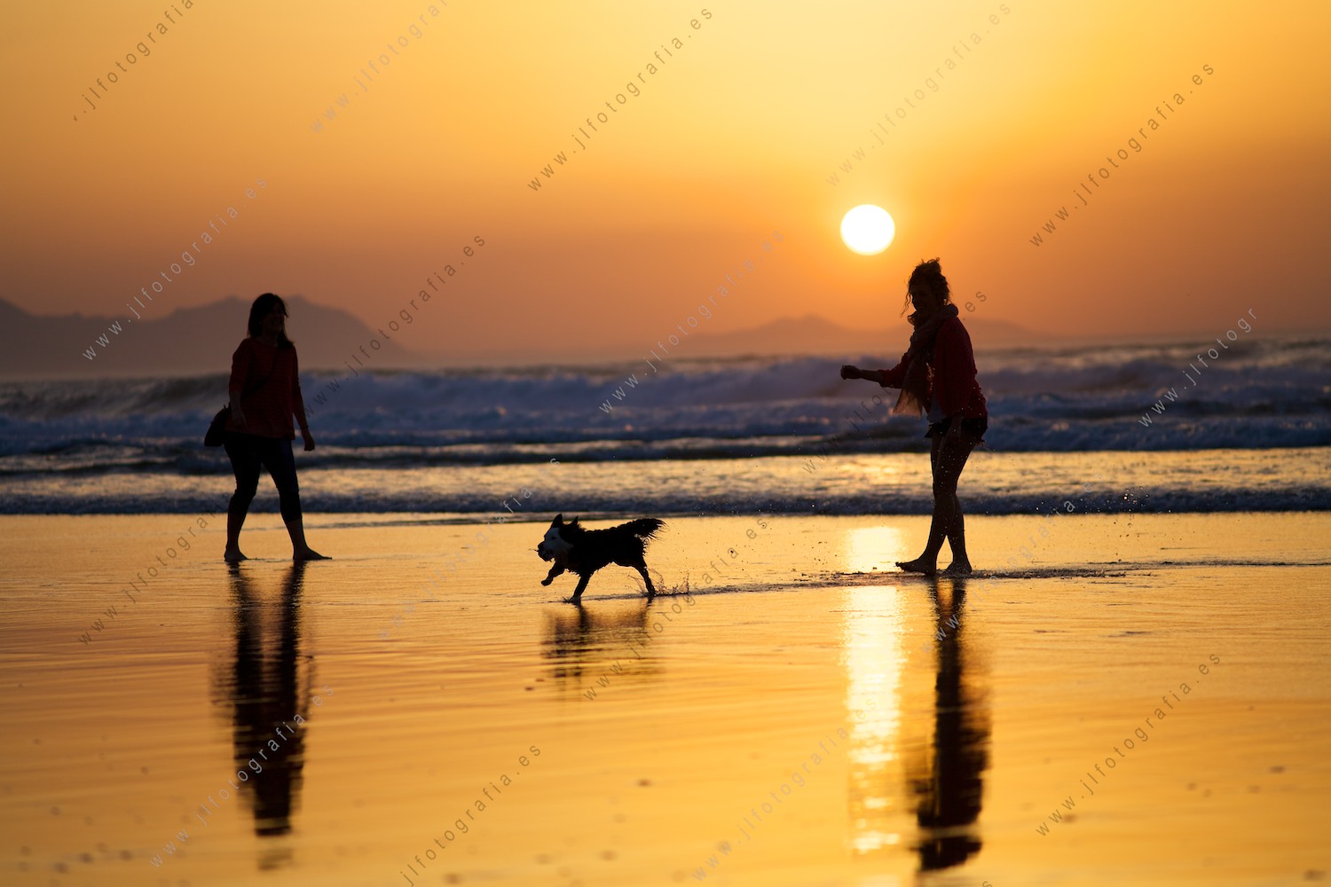 Dos chicas jugando con un perro durante la puesta de sol en la playa de Sopelana