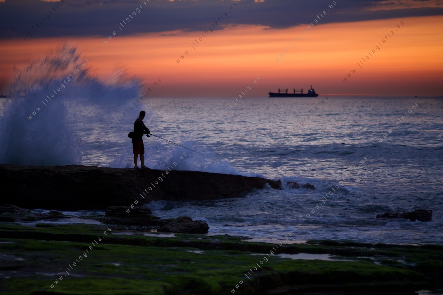 Pescador sorprendido por una ola en las rocas durante el ocaso