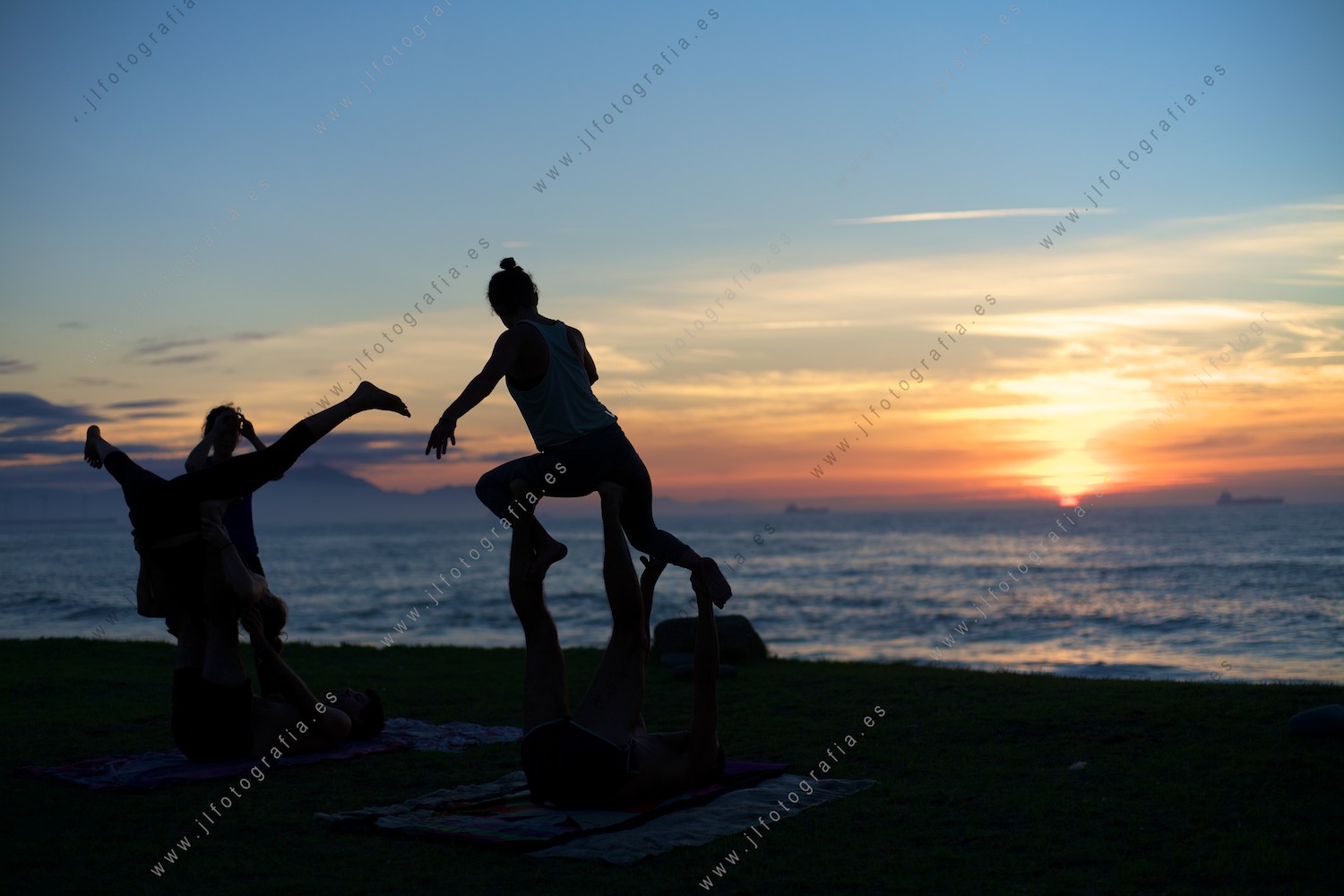 siluetas de gente practicando acroyoga en la playa de Azkorri durante el ocaso.