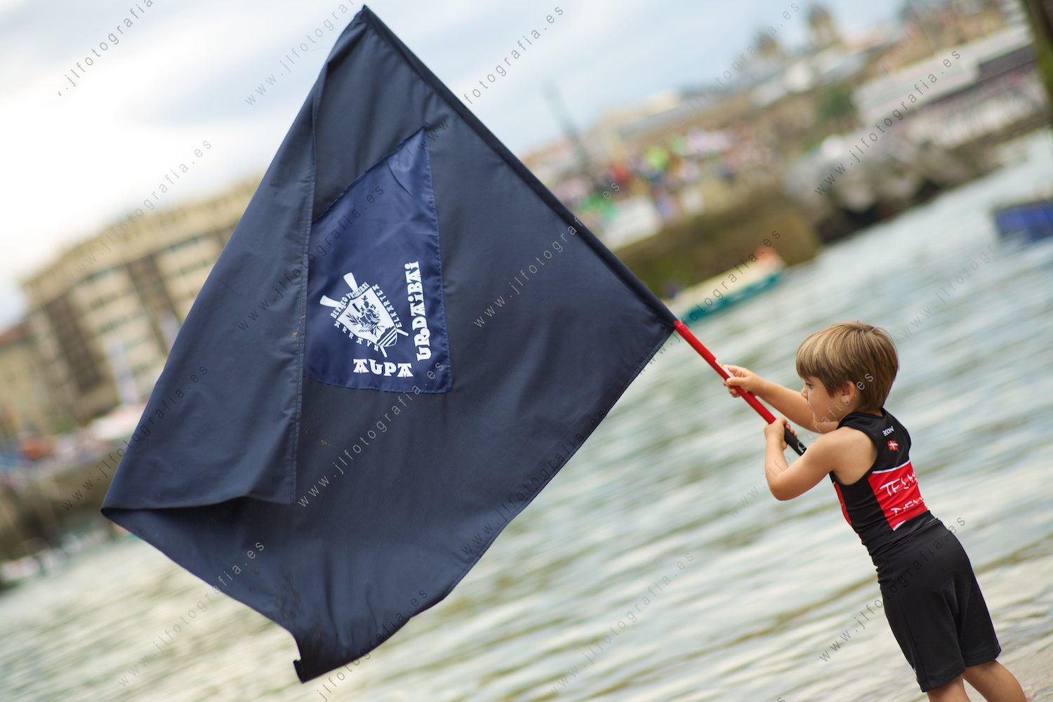 Un niño enarbola la bandera del club de remo Urdaibai durante la regata de bandera de la Concha de Donostia