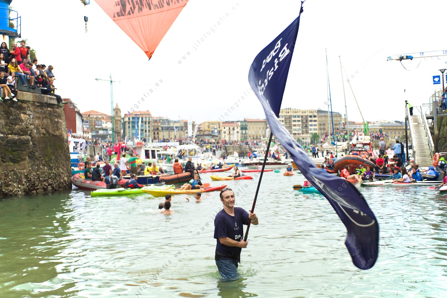 Un seguidor de Urdaibai, ondea desde el agua, la bandera de Bermeo esperando la llegada de la tripulación ganadora de la bandera de la Concha de Donostia
