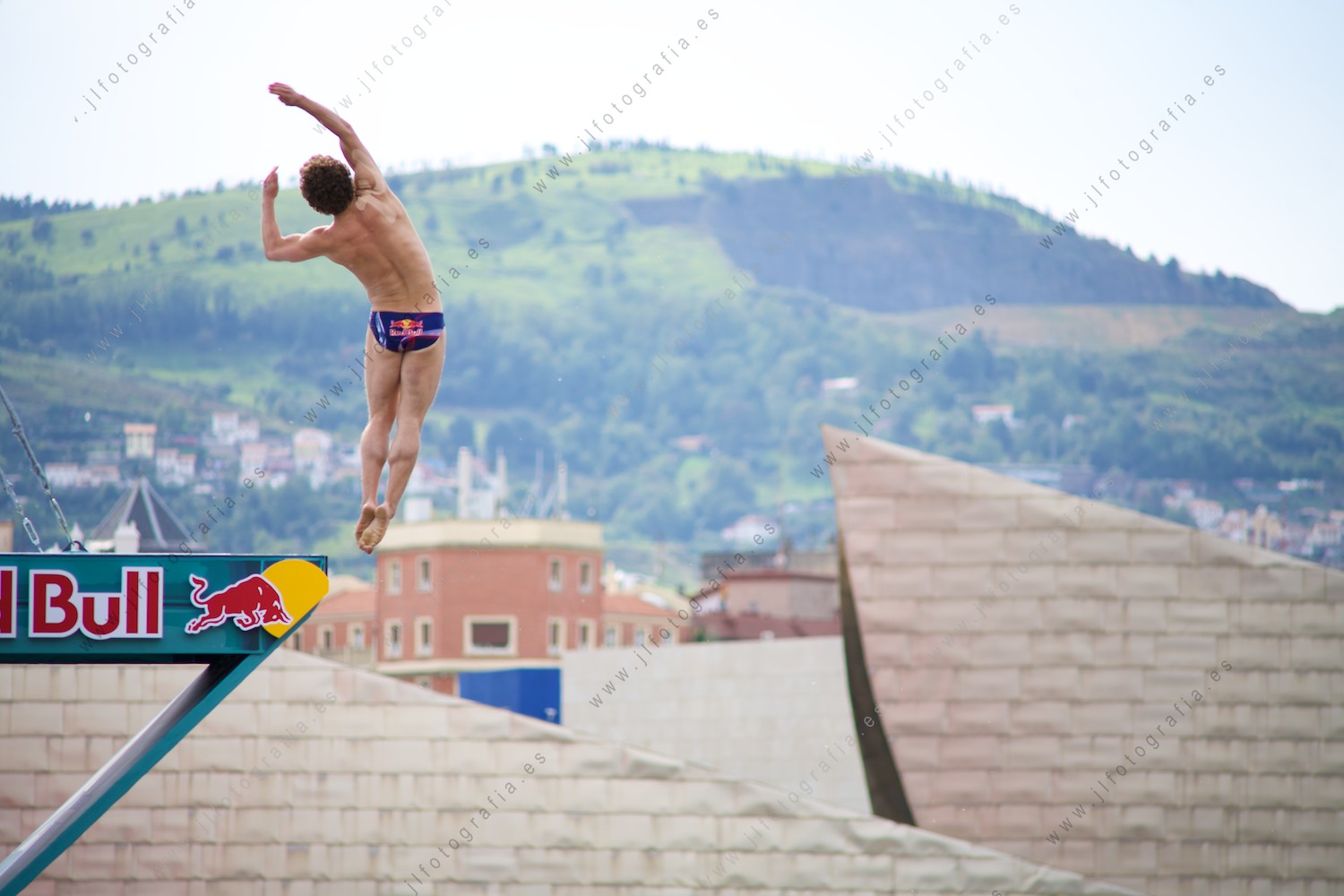Inicio del salto de un clavadista en el Red Bull Cliff Diving de Bilbao con su skyline de fondo
