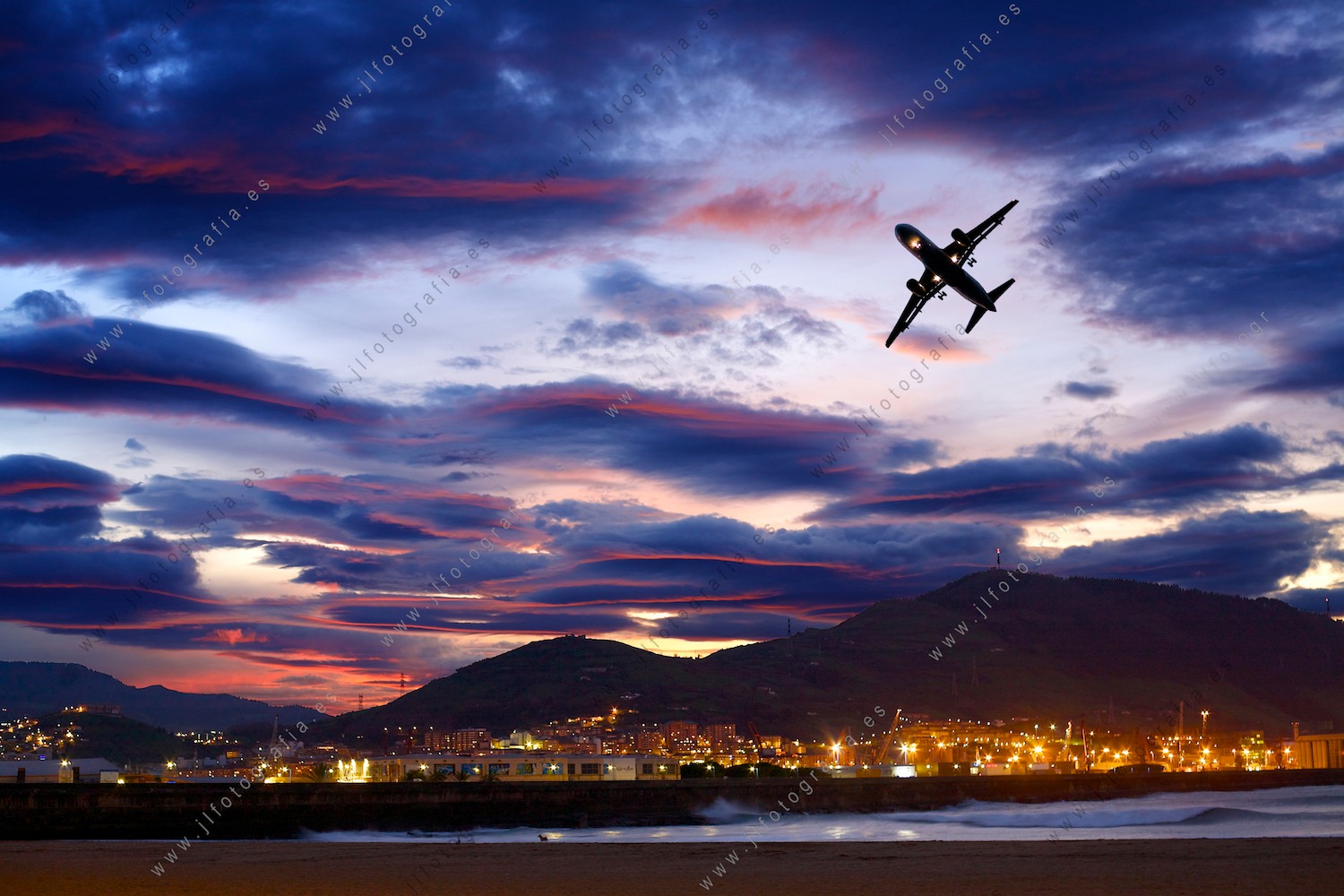 Ocaso desde el paseo de Algorta, con Santurtzi al fondo y un avión virando en el cielo.