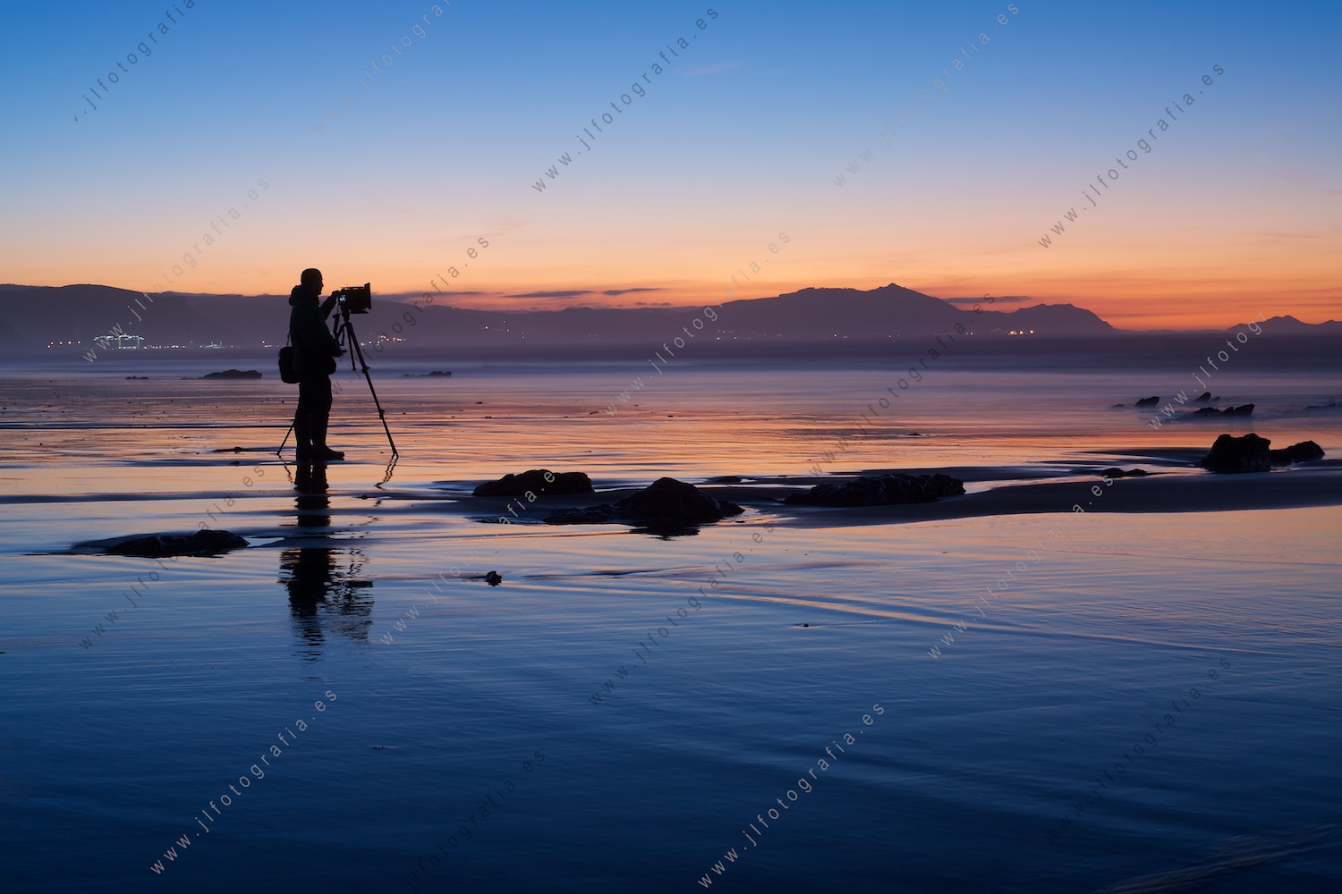 Fotógrafo en la orilla de la playa de Sopelana con un trípode en el ocaso.