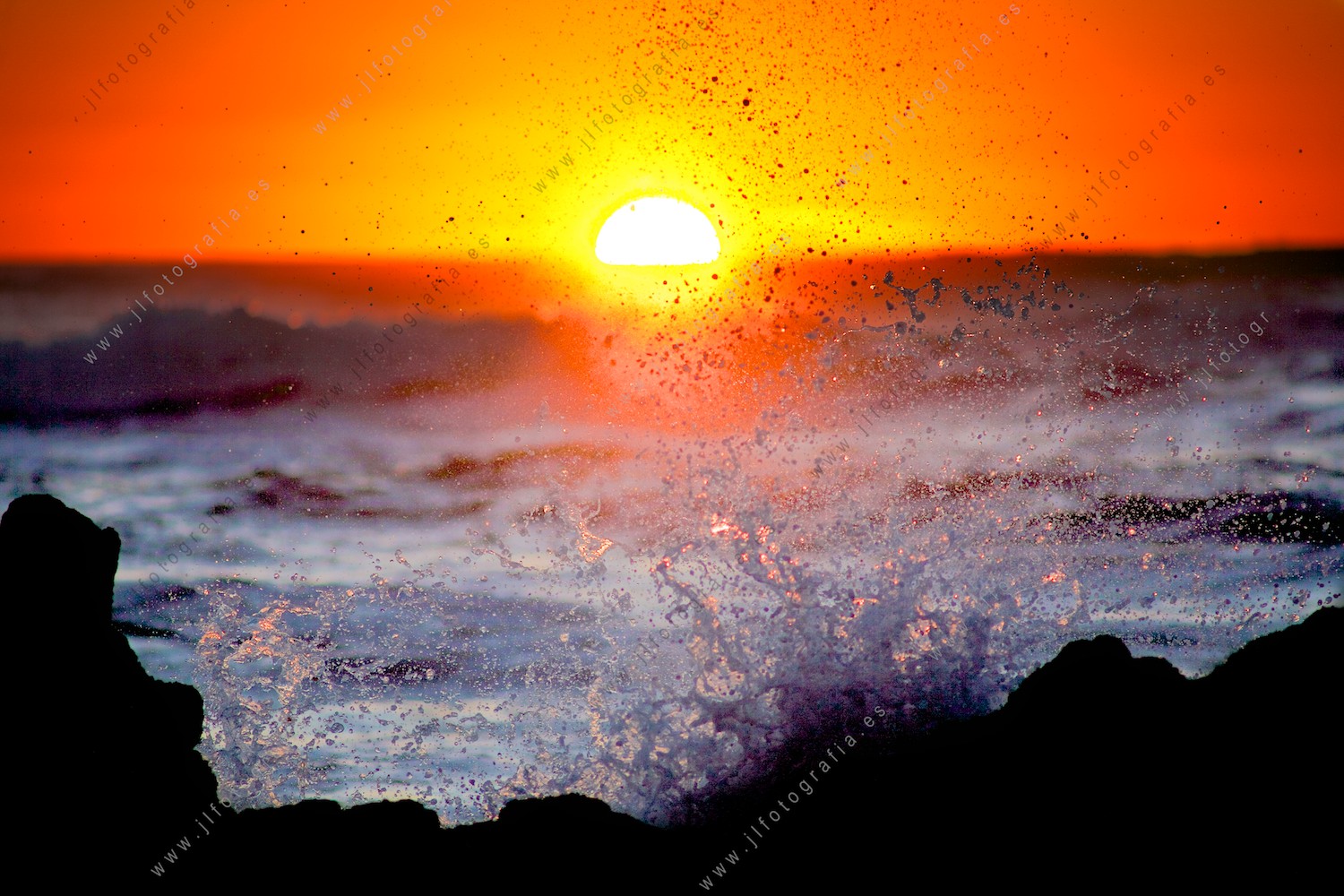escena de verano con las olas rompiendo en las rocas en la puesta de sol.