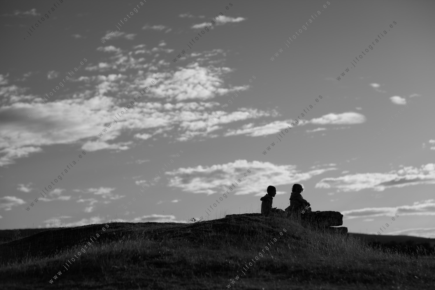 Dos niños miran el horizonte sentados en un pedestal.