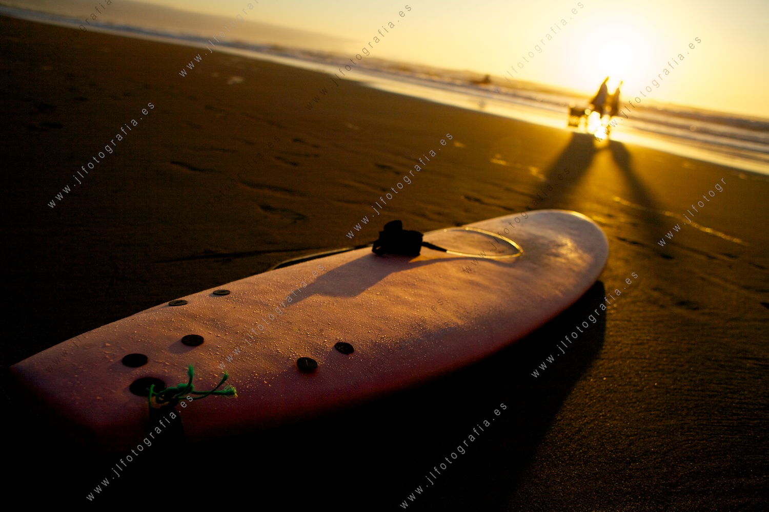 Tabla de surf sobre la arena en el ocaso