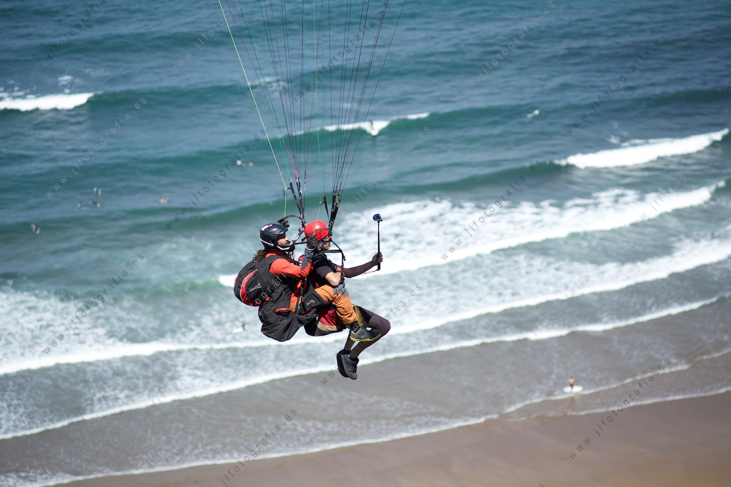 Detalle de parapentistas volando sobre las olas del mar llegando a la playa 