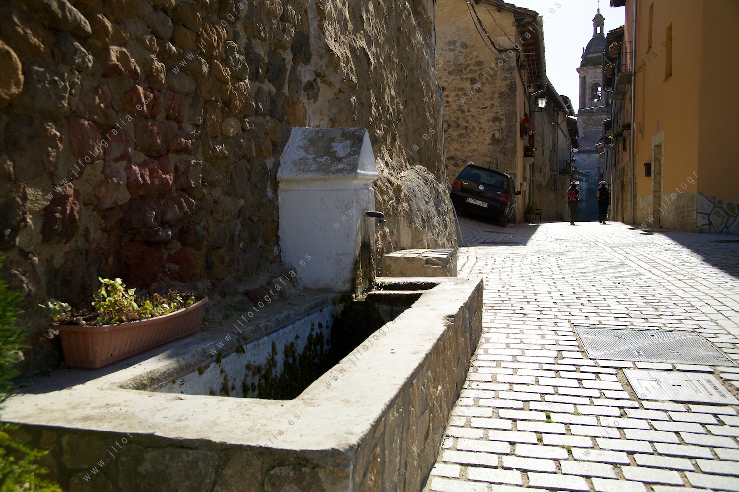 Fuente en una de las calles de Antoñana, en Araba, con la iglesia al fondo