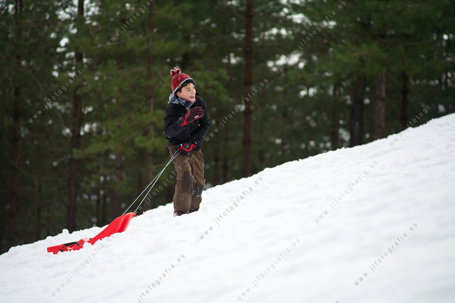Niño subiendo por el monte nevado tirando de su trineo