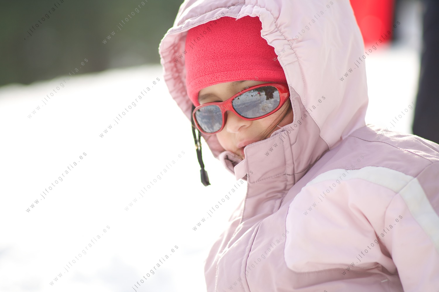 Retrato de gran primer plano de una niña con gafas de sol y ropa de invierno en la nieve
