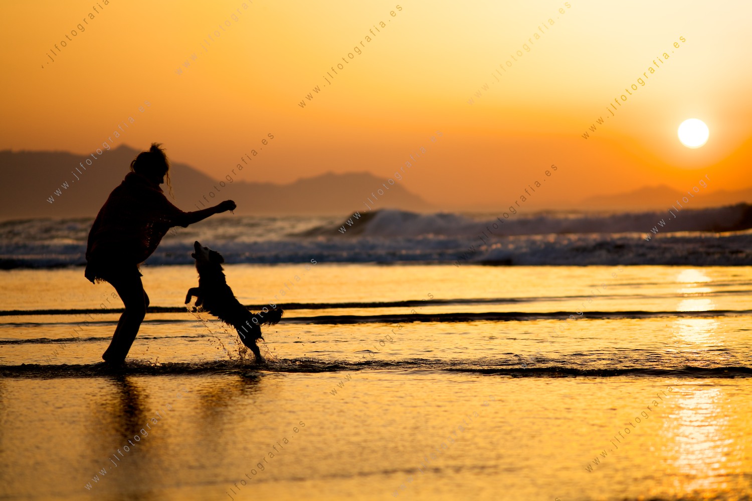 Chica jugando con un perro durante la puesta de sol en la playa de Sopelana 