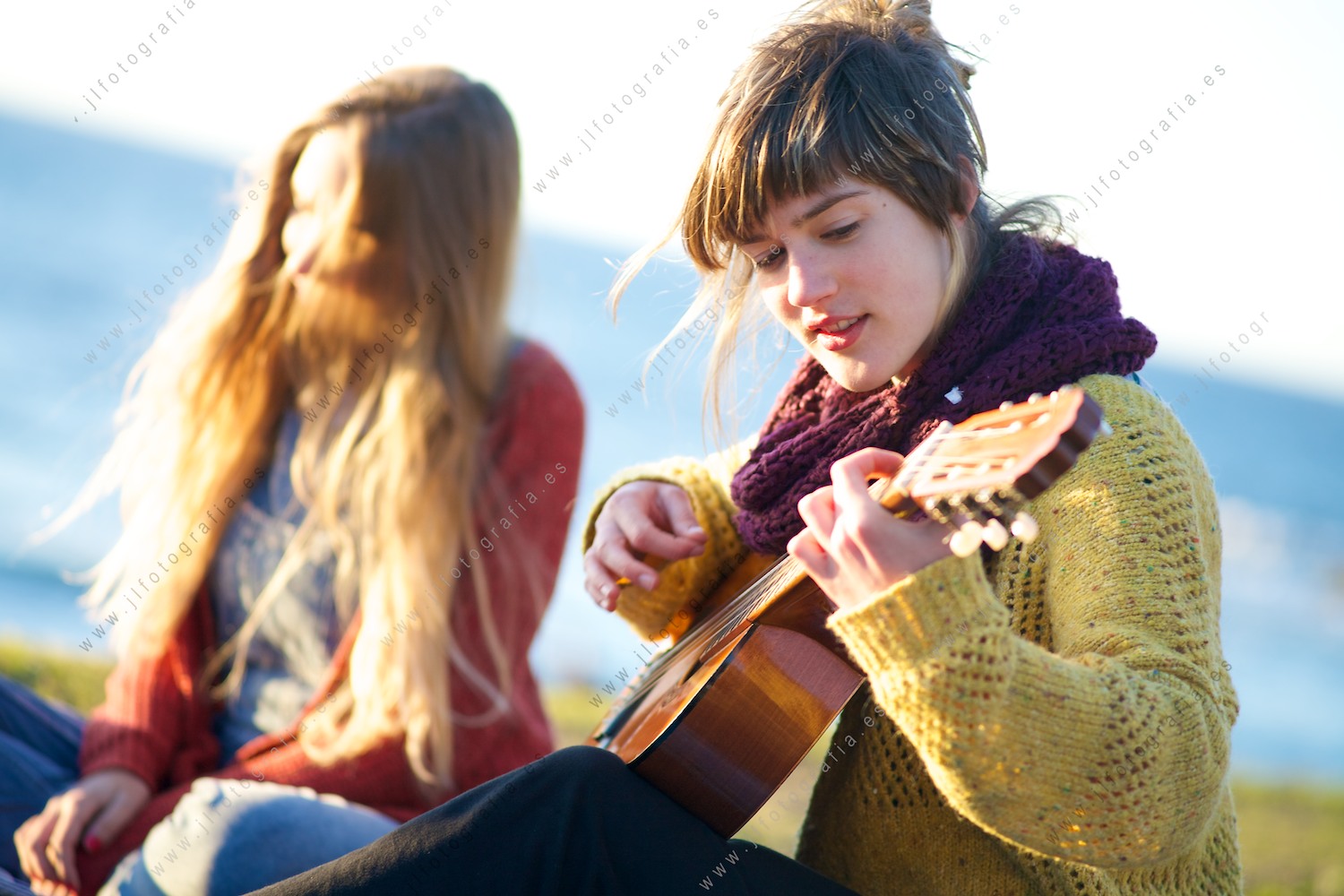 Primer plano de una preciosa joven tocando la guitarra en la playa de Azkorri al atardecer
