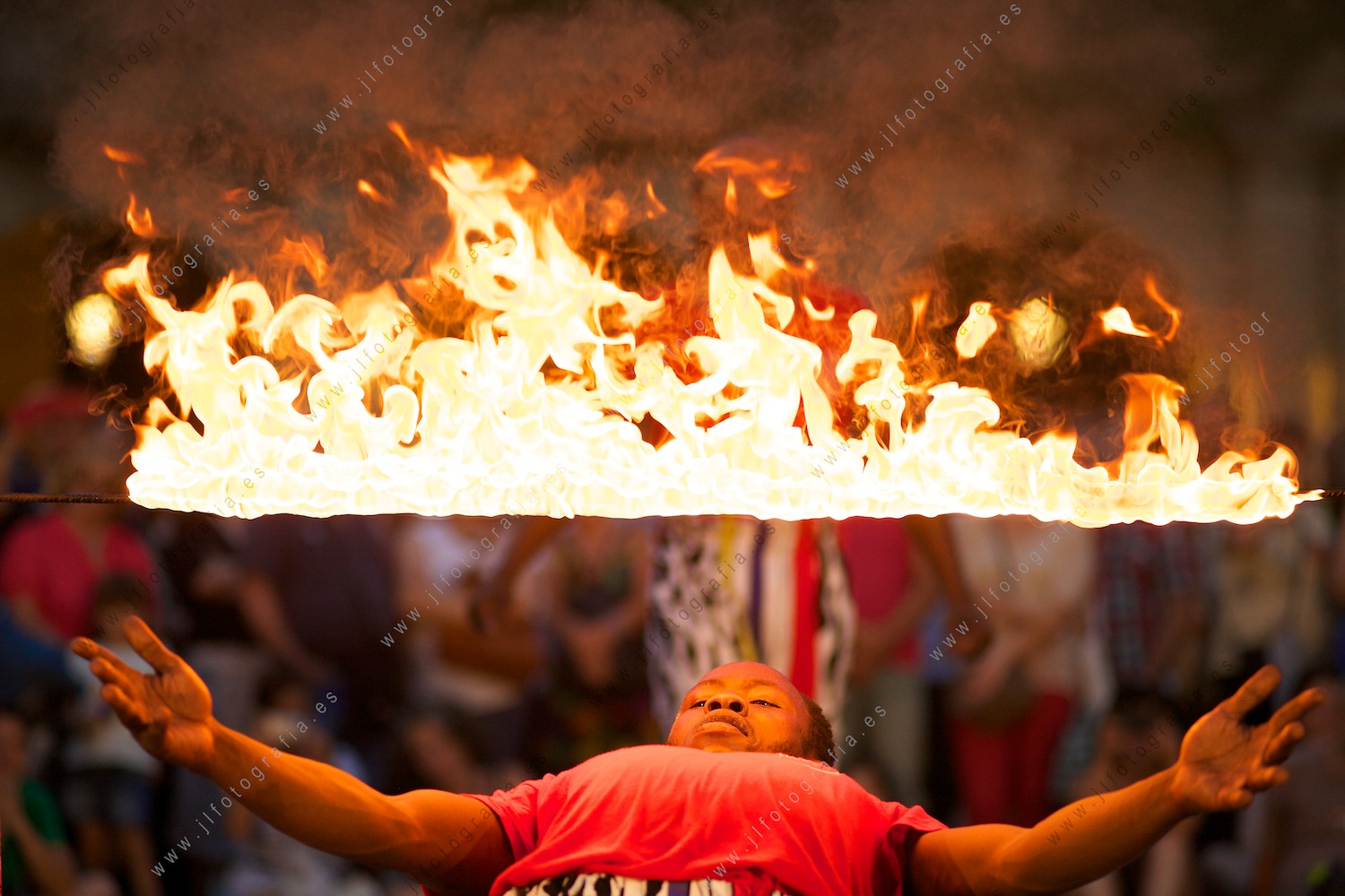 Acróbata pasando en equilibrio bajo una barra de fuego en llamas