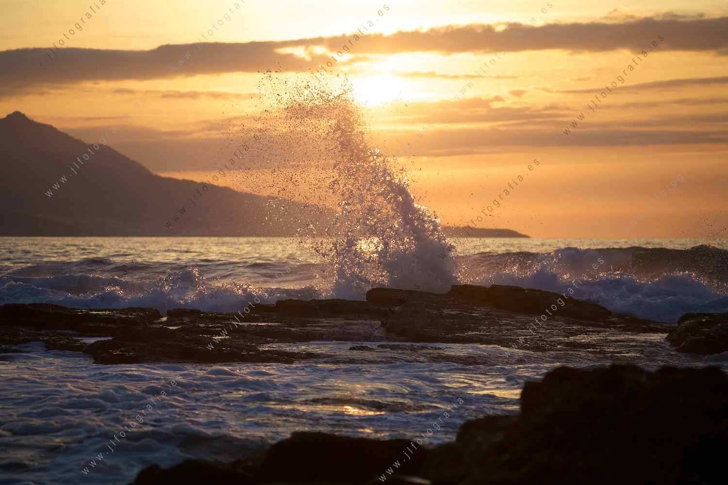 Una ola rompe entre las rocas y alcanza unos metros de altura durante la puesta de sol