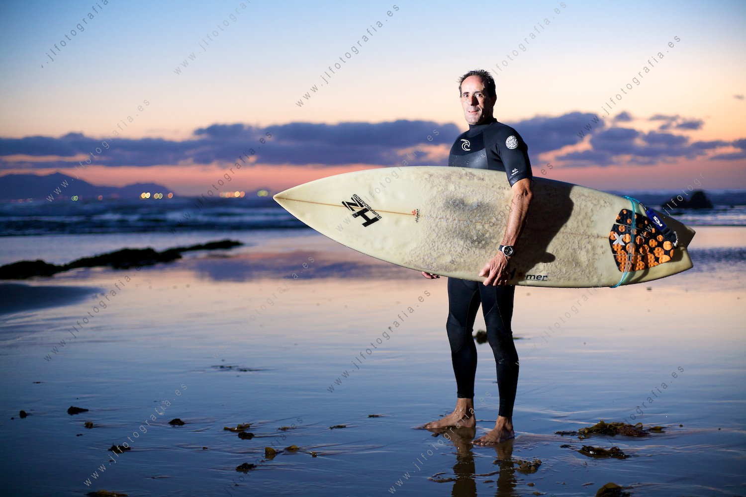 Surfista posando con su tabla de surf en el ocaso del día en la playa de Sopelana