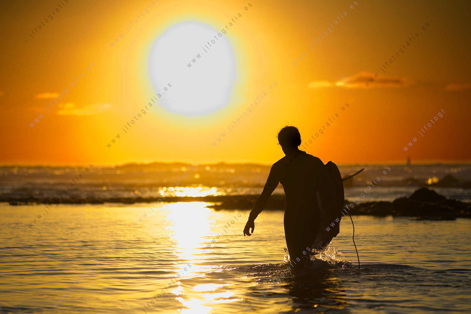 Surfista entrando al agua en busca de olas en la puesta de sol