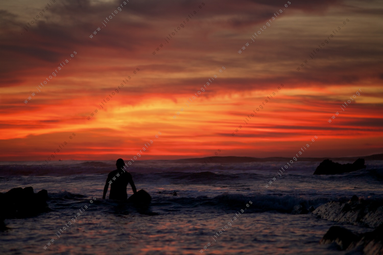 Puesta de sol espectacular con colores de infierno y surfista en busca de olas