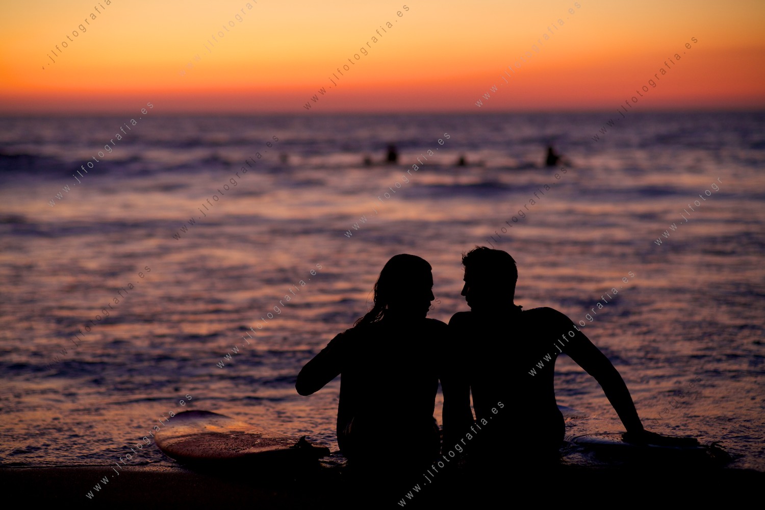 retrato de una pareja de surfistas sentada en la orilla de la playa de Sopelana, a la hora del ocaso