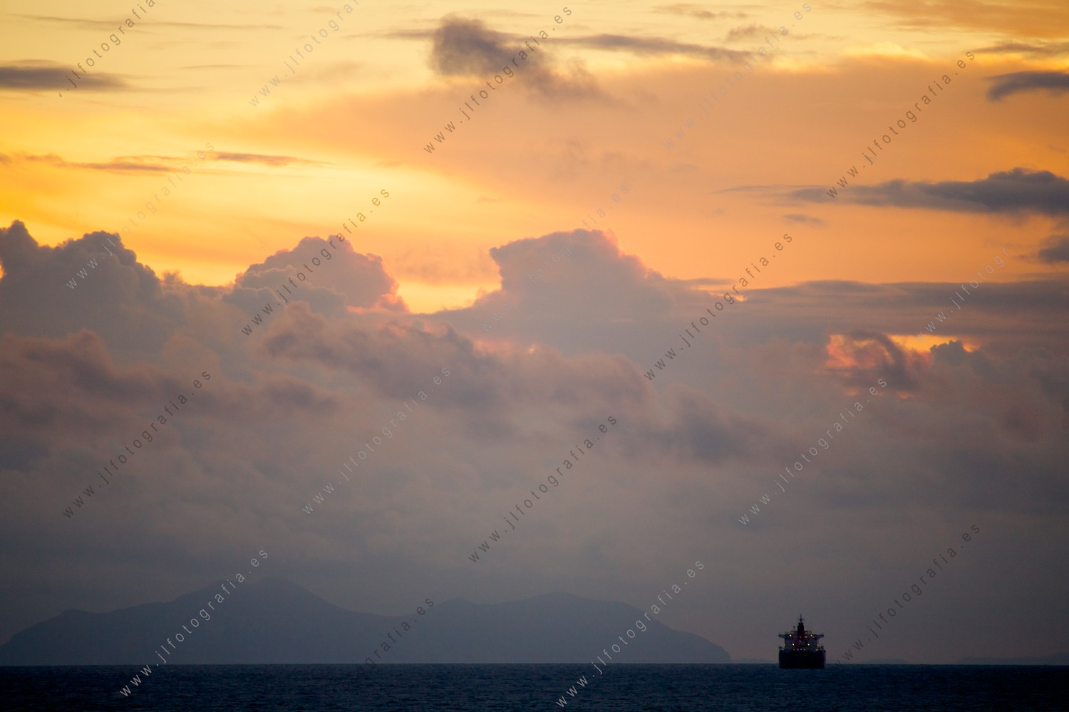 Un barco carguero con vistas al ocaso en un cielo de oro.