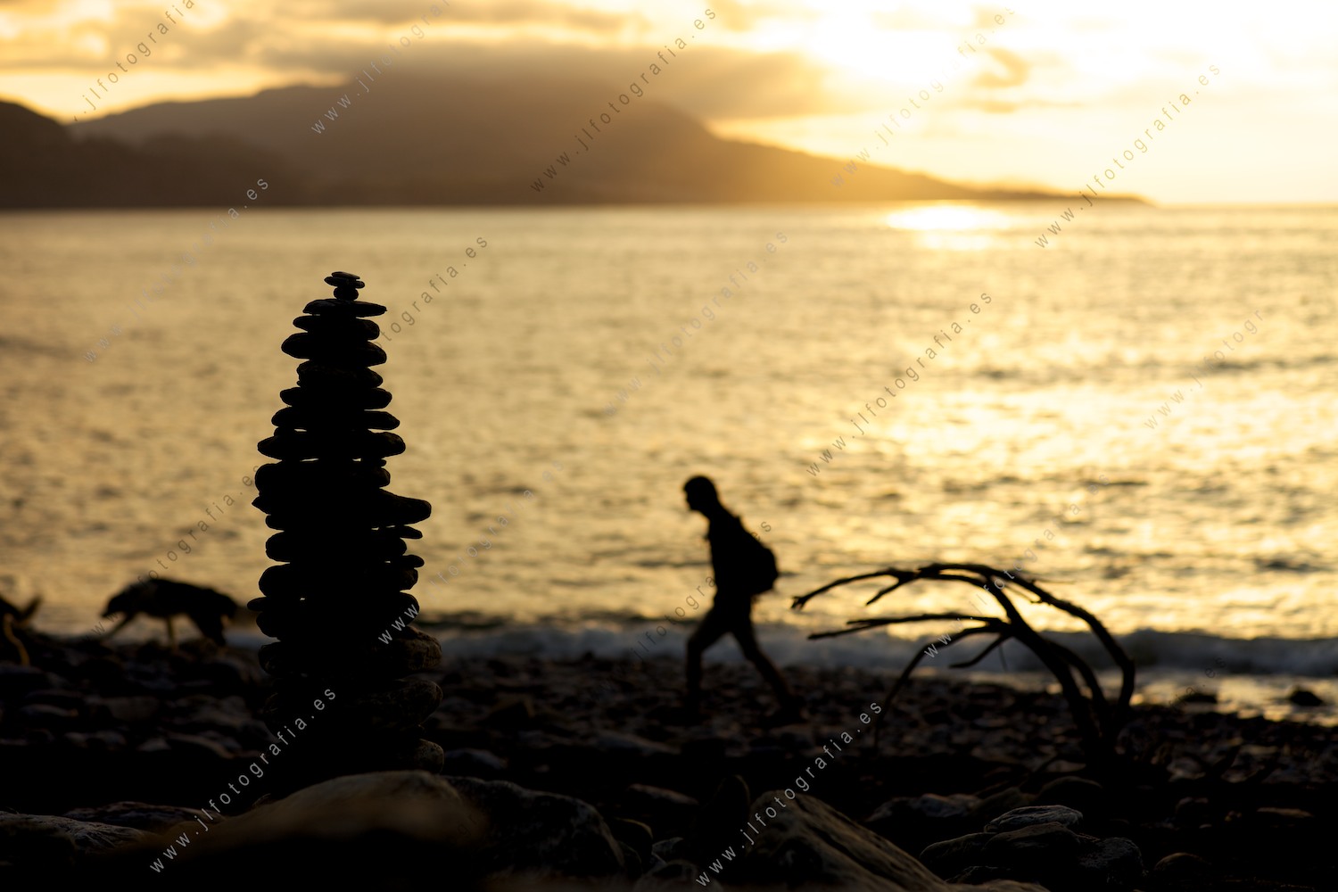En el atardecer, un hito de piedras observa como pasea un hombre y su perro por la playa de el Lastrón, Muskiz.