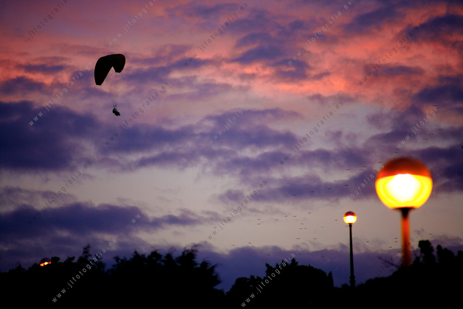 Un parapente vuela por el cielo de color malva con la luz del crepúsculo.