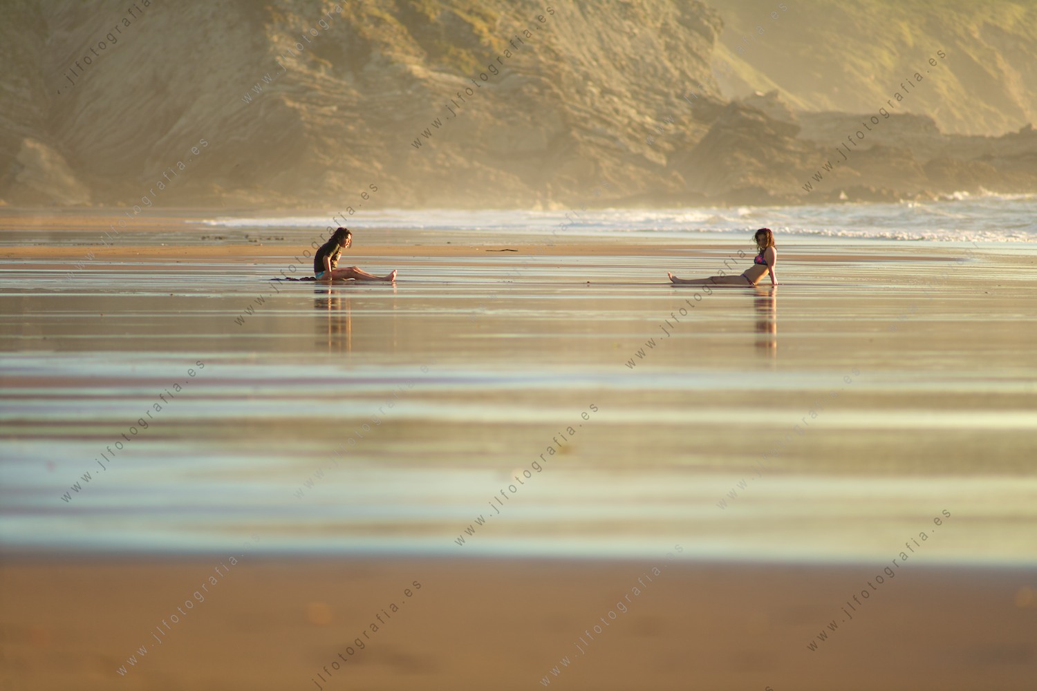 Dos jóvenes juegan en la orilla de la playa, sentadas esperando las olas