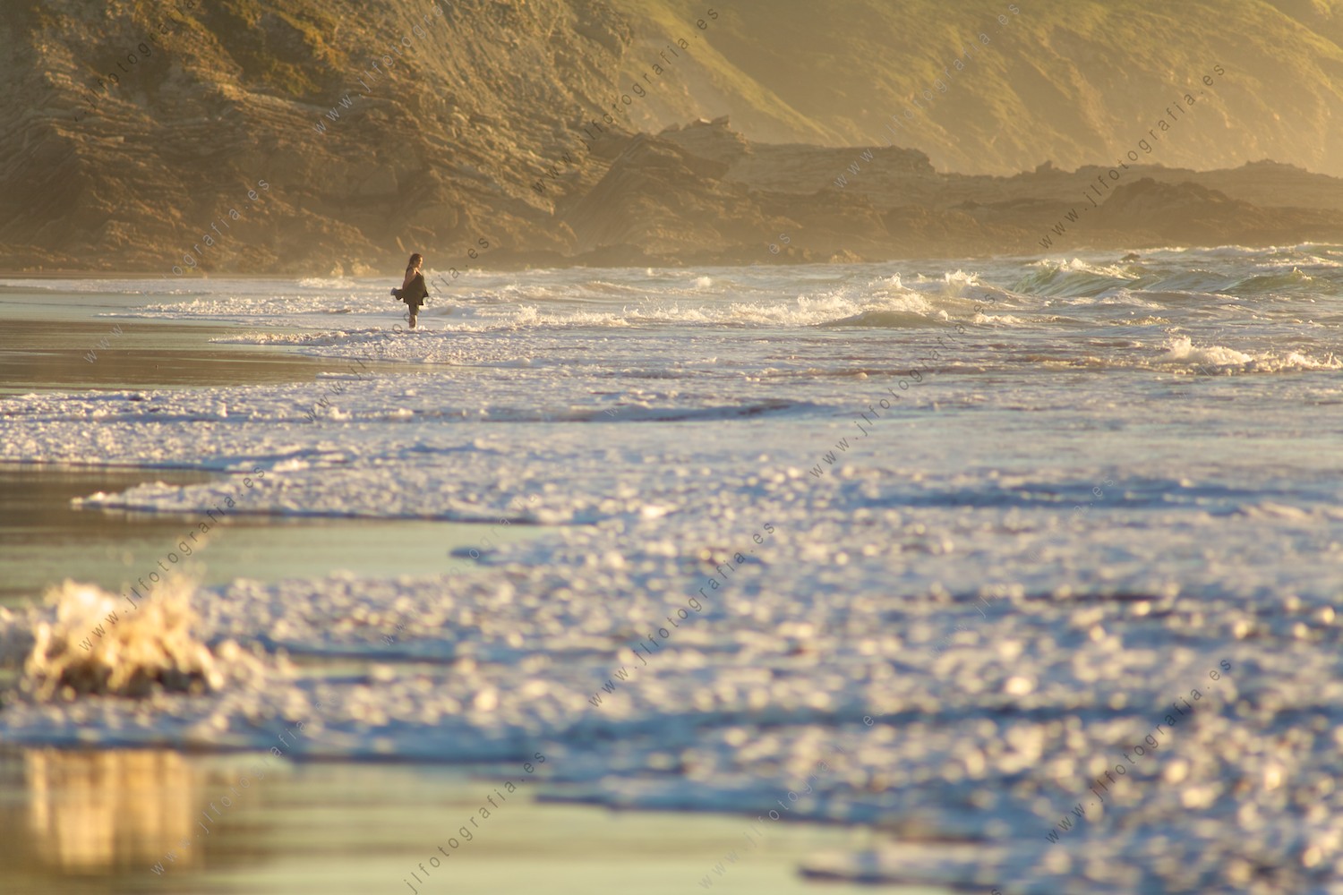 Una mujer observa desde la orilla en la playa cómo le llegan las olas
