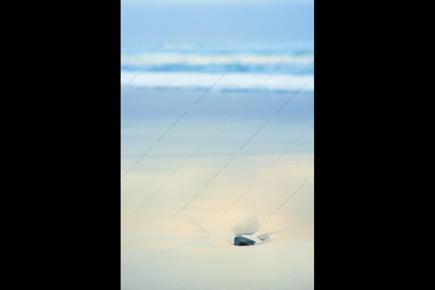 Detalle de una escena de playa con una piedra en la arena.