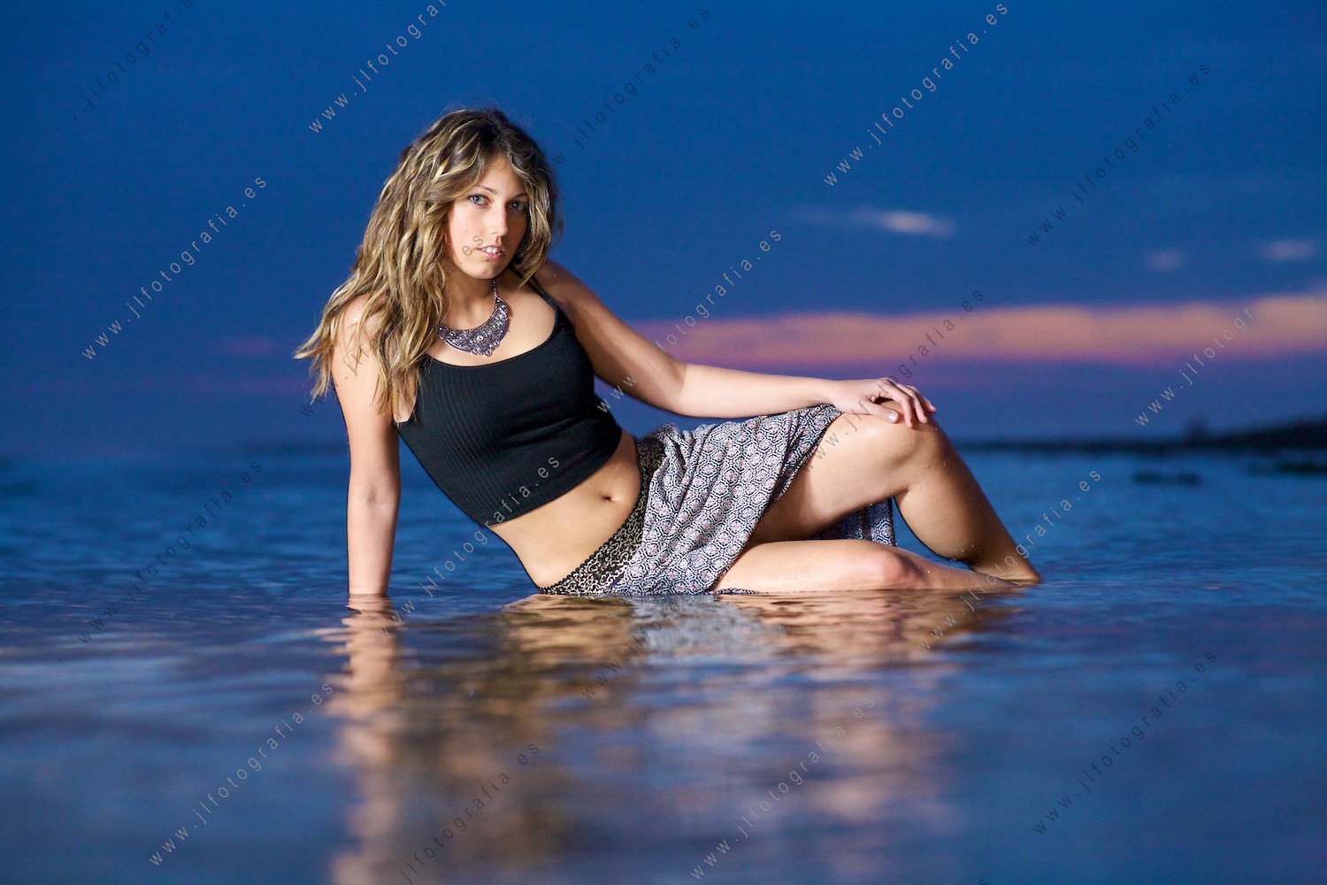 Modelo femenina posando en la playa en la hora azul en un trabajo sesión de iluminación exterior